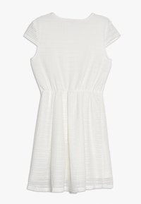 Vit klänning med korta ärmar, resår i midjan och texturerat tyg med subtila vågmönster. Knälång A-linje siluett.