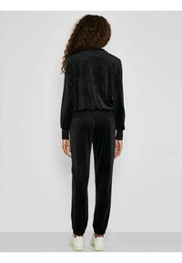Tuta in velluto nero composta da una maglietta a maniche lunghe e pantaloni a gamba affusolata. Il tessuto ha una superficie liscia, con polsini e vita elasticizzati.