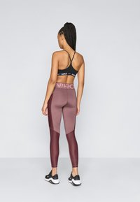 Soutien-gorge de sport Nike avec bretelles ajustables, associé à un legging taille haute composé de panneaux mélangeant maroon et rose ainsi que de sections texturées.
