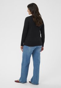 Black long-sleeve shirt with lace detailing on sleeves, paired with light blue wide-leg jeans and maroon flat shoes, viewed from the back.