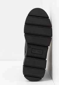 Semelle de chaussure noire avec de larges rainures horizontales et un marquage de taille 37, photographiée sur un fond blanc en coin.