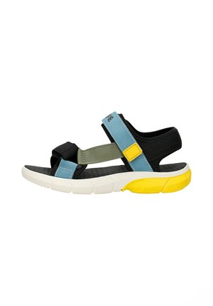 Offene Kindersandale mit schwarzen, blauen und grünen Riemen, einer weißen Sohle und einem gelben Absatz, seitlich betrachtet.