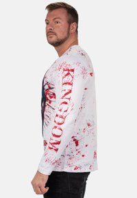 Witte langekmouw shirt met grafisch ontwerp, voorzien van rode spetters, vetgedrukte zwarte letters en een kleurrijke centrale print. Gestructureerde stof.