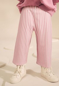 Pantalones a rayas rosas y blancas confeccionados en tejido suave, con un corte holgado y puños rematados, combinados con zapatillas altas blancas.