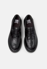 Schwarze Lederschuhe mit abgerundeter Form und dicker Sohle. Verziert mit Brogue-Details und einem breiten Klettverschlussriemen über der Vorderseite.