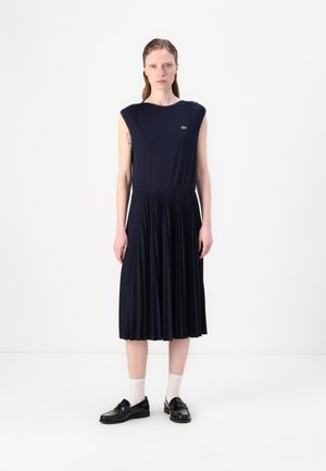 Navy pleated dress with sleeveless design, made of soft fabric. Features a round neckline and small embroidered logo on the chest.