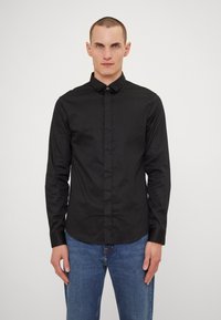 Camisa negra de botones con cuello estructurado y mangas largas, hecha de una tela suave, combinada con jeans de mezclilla azules.