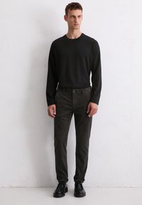 Chemise noire à manches longues, pantalon en velours côtelé gris et chaussures noires à lacets. Design minimaliste avec des textures lisses et une coupe décontractée.