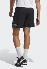 Pantalones cortos deportivos negros con rayas blancas y coloridas en el lado izquierdo, llevados con calcetas blancas y zapatillas deportivas negras.