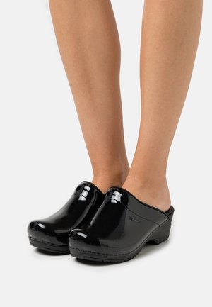 Black patent clogs with a rounded toe, open back, and textured sole. Features a slight heel and smooth glossy finish.