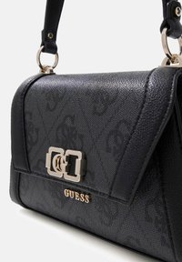 Borsa nera con materiale testurizzato, design con pattina piegata, dettagli in metallo color oro e nome del marchio "GUESS" sulla parte anteriore.