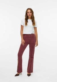 Top blanco de algodón de manga corta combinado con pantalones de pana burdeos acampanados. La modelo lleva zapatos de tacón alto marrones con detalles decorativos.