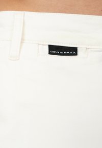 Witte kleding met een gladde textuur, met een zichtbaar etiket waarop "CIPO & BAXX" in zwart staat op een contrasterende achtergrond.