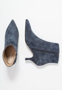 Botín de ante azul marino con puntera puntiaguda, cremallera lateral y tacón de 4 cm; textura suave con acabado mate.