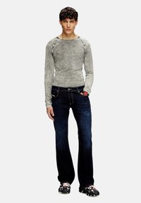 Camisa de manga larga gris ajustada con un acabado texturizado, combinada con jeans acampanados de color azul oscuro. Destaca un acento rojo en el bolsillo de los jeans.