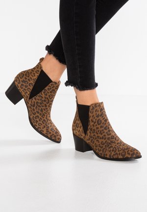 Kvinde iført brune ankelstøvler med leopardmønster, sorte elastiske sidepaneler og blokhæle, kombineret med sorte skinny jeans med frynset kant.