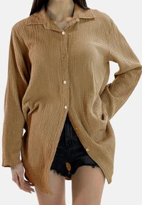 Chemise marron à boutons en tissu texturé, avec col à rabat et poches latérales, coupe décontractée et ourlet arrondi.