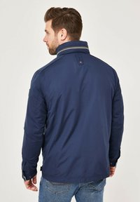 Navy blue jacket featuring a high collar, button cuffs, and subtle striped detailing on the collar. Lightweight material with a smooth texture.