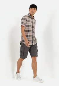 Kurzarm-Hemd aus Karomuster in Grau, Orange und Weiß; kombiniert mit grauen Cargo-Shorts mit Taschen; weiße Sneakers runden das Outfit ab.