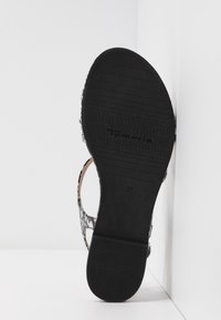 Semelle noire d'une sandale avec une texture antidérapante. La partie supérieure de la bride affiche un motif serpent noir et gris clair. Taille marquée comme 37. Étiquette de marque visible.