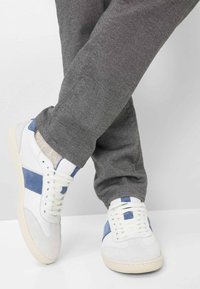 Białe sneakersy z niebieskimi zamszowymi akcentami, teksturowane szare spodnie i kremowe podeszwy. Szczegółowe przeszycia i klasyczny design na sznurówki.