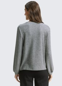 Grey long-sleeve blouse with a diamond pattern, smooth texture, rounded neckline, and elastic cuffs. Styled with black trousers.