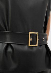 Black faux leather belt featuring a gold rectangular buckle, smooth texture, and decorative studs along the strap.
