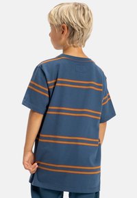 Blauw T-shirt met korte mouwen, oranje horizontale strepen en een ronde hals. Gemaakt van katoen, met een losse pasvorm, label aan de achterzijde van de hals.