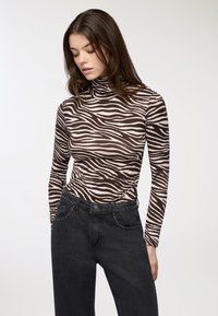 Maglione a collo alto a righe zebrate marroni e bianche abbinato a jeans neri a vita alta con dettagli borchiati lungo le tasche.