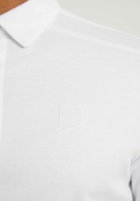 Biała koszula polo wykonana z gładkiej bawełny, z kołnierzykiem i delikatnym haftowanym logo na środku.