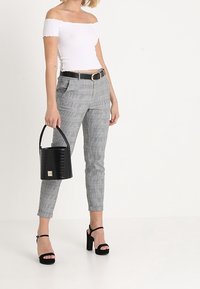 Vit avaxlad topp, grå rutiga tapered byxor, svart bälte, klumpiga klacksandaler och en svart texturerad bucket-väska.
