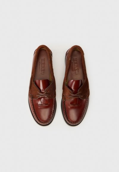 Scarpe in pelle marrone slip-on con accenti in pelliccia, punta arrotondata e lacci decorativi in pelle. Finitura liscia con texture a contrasto.