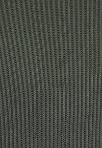Nahaufnahme von dunkelgrauem Strickstoff mit vertikalem Rippmuster und sichtbaren Maschenmustern.