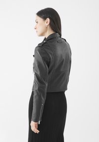 Chaqueta corta de cuero negro con cremalleras, hombreras y mangas texturizadas, combinada con una falda negra acanalada.