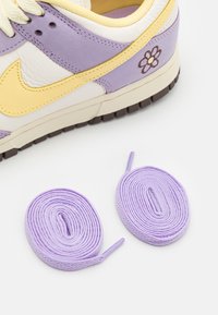 Lila och krämfärgad sneaker med gula accenter, försedd med blommig brodyrdetalj, parat med två lavendelfärgade skosnören, texturerad ovandel.