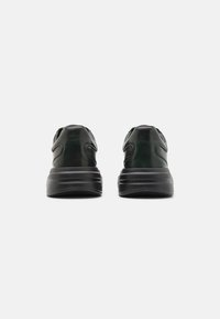 Sneakers neri e verde scuro con una tomaia in pelle liscia, suola in gomma spessa e supporto per la caviglia imbottito, arricchiti da dettagli di cucitura discreti.