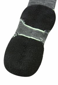 Calzino nero e grigio con una suola nera imbottita. Presenta un corpo a maglia texturizzata e due strisce verde chiaro attraverso la parte centrale.