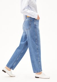 Hellblaue, locker sitzende Jeans mit hohem Bund, fünf Taschen und fransigem Saum. Kombiniert mit weißen, niedrigen Schuhen.