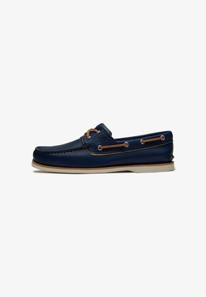 Scarpa da barca in pelle blu navy con lacci marrone chiaro, suola bianca e dettagli cuciti, mostrata di profilo su sfondo bianco.