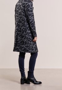 Grijze gestreepte overjas met een iets gestructureerd ontwerp, lange mouwen en een rechte snit. Gekocht met donkerblauwe broek en zwarte haklaarzen.