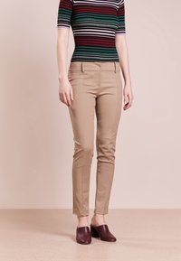 Beige op maat gemaakte broeken met een slim fit, voorzien van voorzakken en een gladde textuur, gecombineerd met donkere klompen en een gestreept shirt.