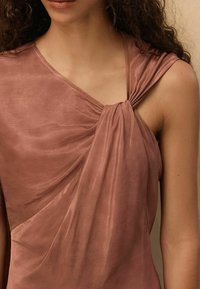 Välsittande ärmlös topp i dammros med en vriden frontknut, som har mjukt, glatt tyg och draperade detaljer, vilket framhäver en elegant silhuett.