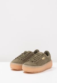 Sneakers in suede verde oliva con suola in gomma traslucida chunky. Presentano lacci e un marchio dorato sul lato. Design con punta arrotondata.