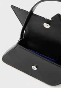 Μαύρη δερμάτινη τσάντα χειρός με τριγωνικό σχήμα, ασημί μεταλλικά στοιχεία και εσωτερικό διαμέρισμα που περιέχει ένα μπλε αντικείμενο. Λαβή προσαρτημένη για μεταφορά.