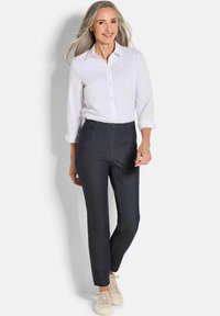 Donkerdenim broek met hoge taille, gecombineerd met een wit overhemd met knopen. De stof heeft een gladde textuur en een getailleerde pasvorm. Versterkt met beige sneakers.