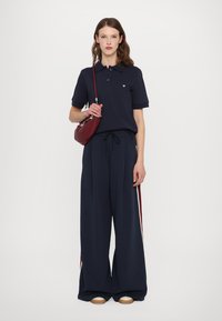 Navy polo shirt with short sleeves, paired with wide-leg navy pants featuring side stripes and a small logo. Accessorized with a burgundy bag.