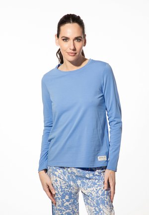 Lichte blauwe langgelegde blouse gemaakt van zachte stof, met een ronde hals en een klein label aan de zoom. Combinatie met gemêleerde blauwe broek.