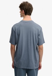 Camiseta azul para hombre con mangas cortas, cuello redondo y tejido texturizado. Presenta un logo sutil en la parte posterior. Diseño minimalista.