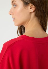 Camiseta roja con cuello redondo y mangas cortas, confeccionada en tejido suave. Presenta un detalle de costura visible a lo largo del hombro.