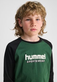 Maglietta a maniche lunghe verde e nera in cotone, con un logo in testo bianco, design sportivo con scollo tondo e maniche raglan.